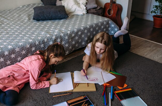 Photo two girls friends play at home draw with pencils and felt-tip pens and have fun