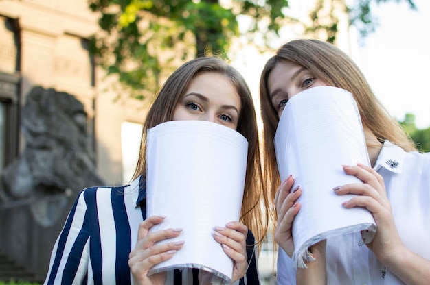 2人の女の子が書類を手に学校に行く 学生はレッスンを学び、顔を覆う