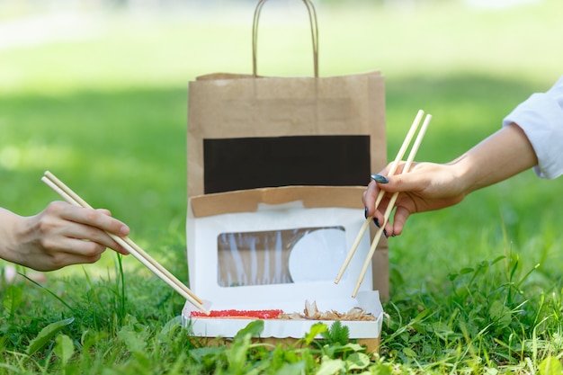 Two girls have a dinner with japanese sushi roll on on a summer picnic