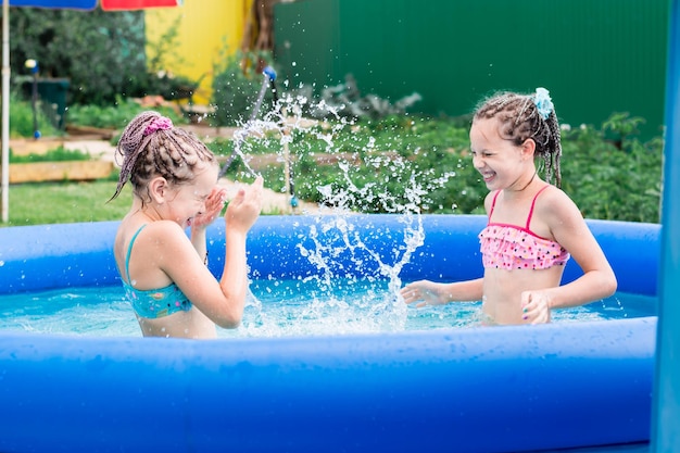 Two girls have fun splashing in an inflatable pool on a summer day in the backyard