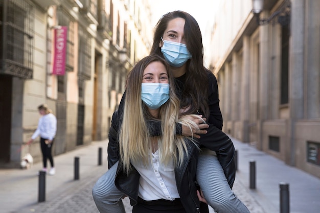 Two girls having fun on the street. They are wearing medical masks.