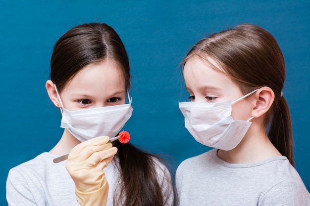 医療用マスクを着た2人の女の子が、1人がピンセットで保持しているコロナウイルスを調べています。ラテックスの手袋をはめてください。肺炎のパンデミック