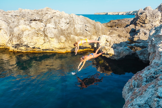 Two girls jump into the sea water from a cliff