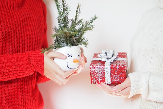 Two girls in knitted woolen sweaters in white and red give each other gifts.