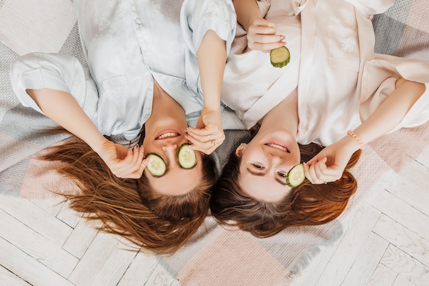 Two girls make homemade face and hair beauty masks. Cucumbers for the freshness of the skin around the eyes 