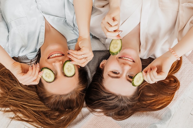 Two girls make homemade face and hair beauty masks. Cucumbers for the freshness of the skin around the eyes 