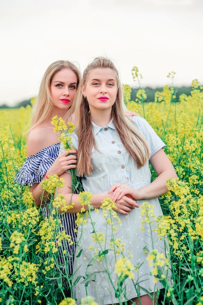 Две девушки модели позируют вместе на камеру в поле рапса