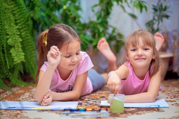 Two girls paint with paints lying on the floor at home or in kindergarten