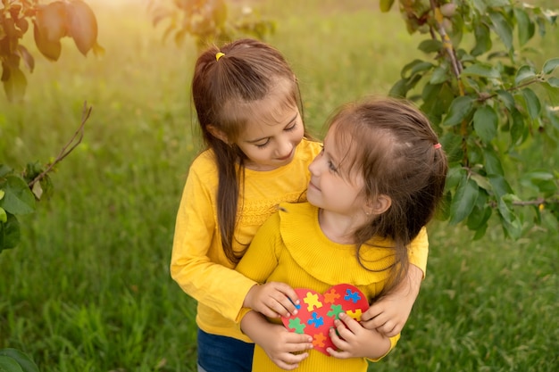 Two girls in the park hugging each other holding a heart made of puzzles