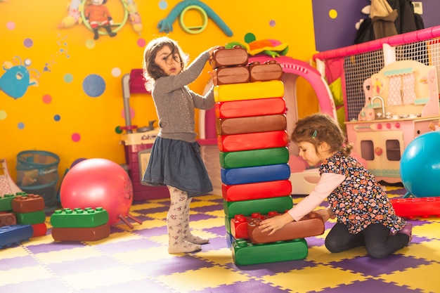 Two girls play with big bricks in playroom