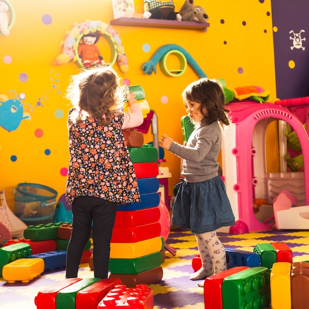 Two girls play with big bricks in playroom