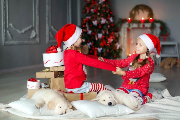 Two girls in red caps santa claus hug and give each other gifts