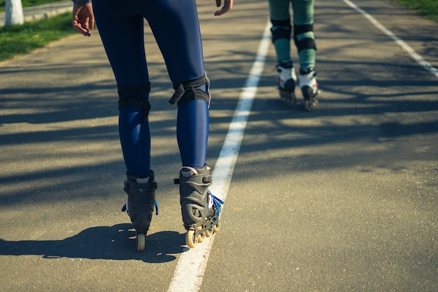 Two girls on roller skates ride along the road Sport girls One girl is ahead of the other