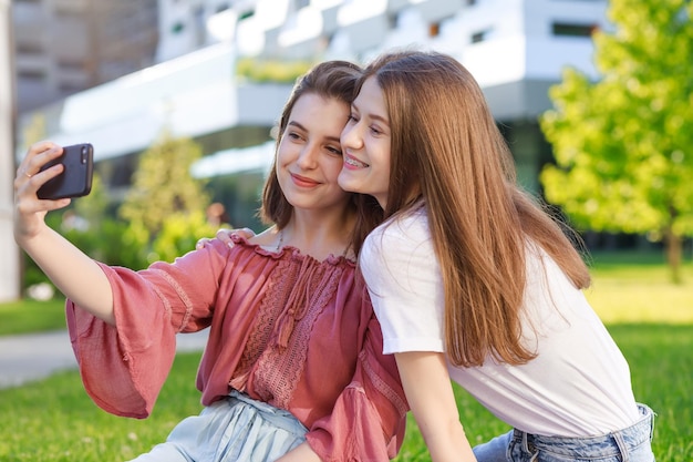 Two girls schoolgirls in the summer in a city park take a self