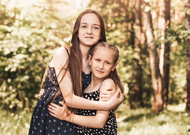 Two girls sister hugging and smiling on the nature in the summer