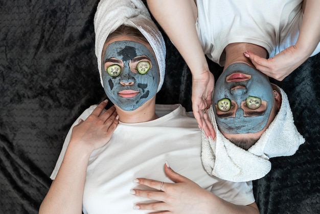 Two girls or sister make clay facial mask with fresh cucumbers on her eyes lying on the floor