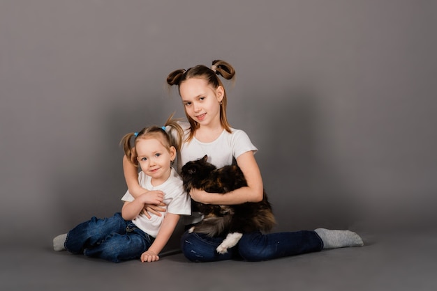 Two girls sisters hugging black cat in a studio