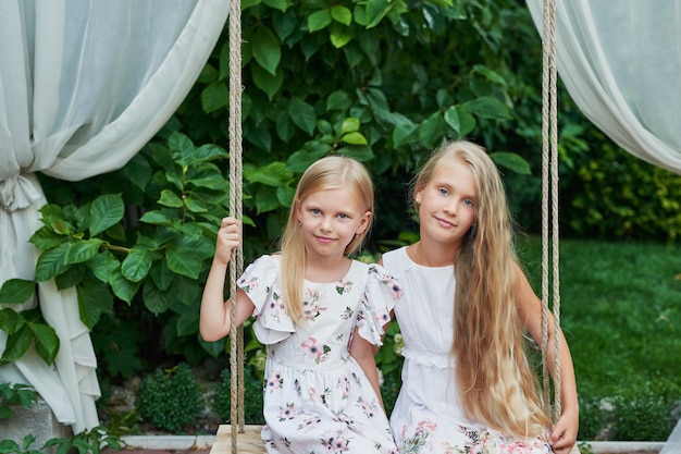 two girls sisters ride on a swing in the summer in the garden