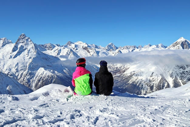 Two girls sit on top of a snowy mountain