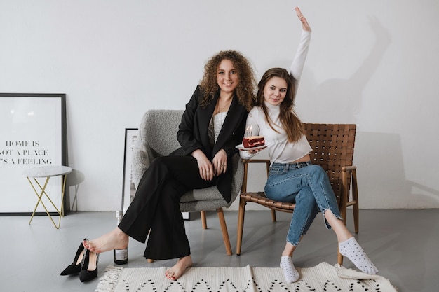 Two girls sitting in the studio on chairs with a cake