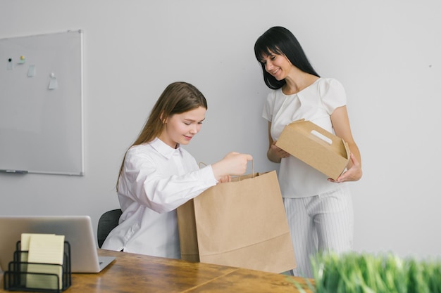 2 人の女の子が微笑み、バッグや食品用の箱などのクラフト パッケージを手に持っています。