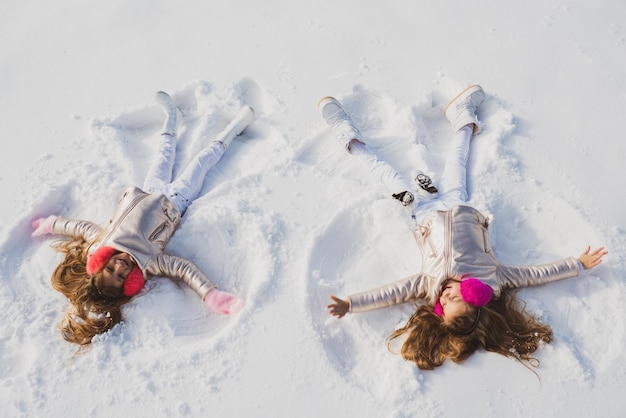 スノーエンジェルの2人の女の子は、コピースペースの子供たちが遊んでいる雪の上に横たわっている笑顔の子供たちを示しています...