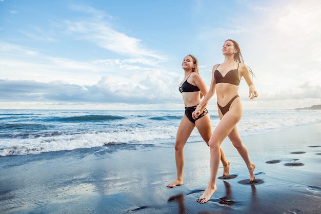 Two girls in swimsuits run on the beach