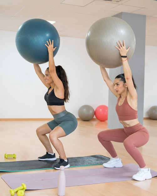 TWO GIRLS TRAINING YOGA AND PILATES TOGETHER WITH A BALL AND WEIGHTS