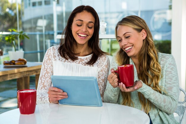 Two girls use a tablet while drinking tea