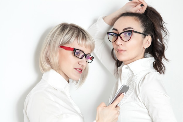 Two girls in white shirts and glasses do selfie on the phone