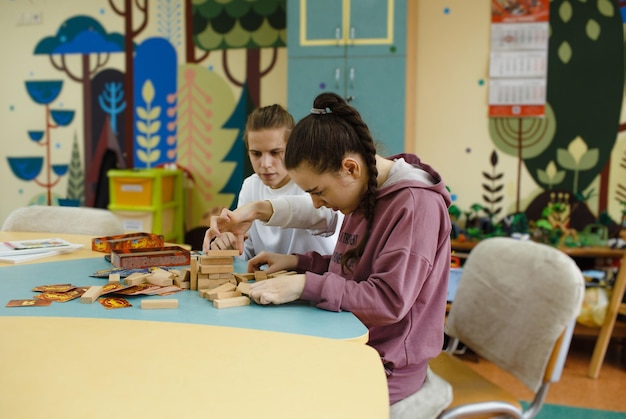 Photo two girls with disabilities are playing jenga sitting at a large table