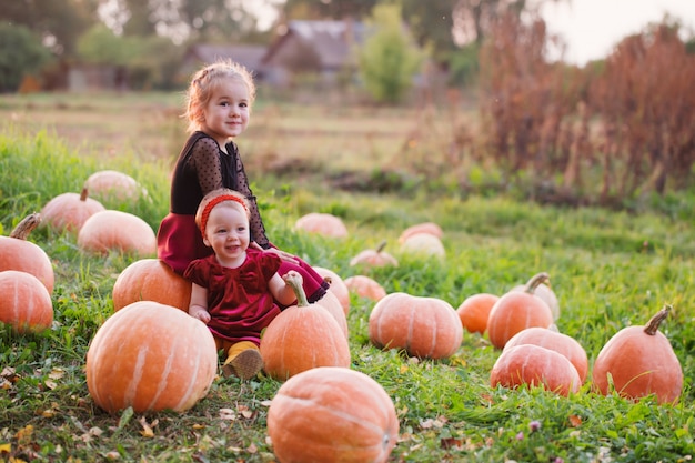 Two girls with pumpins on field at sunset