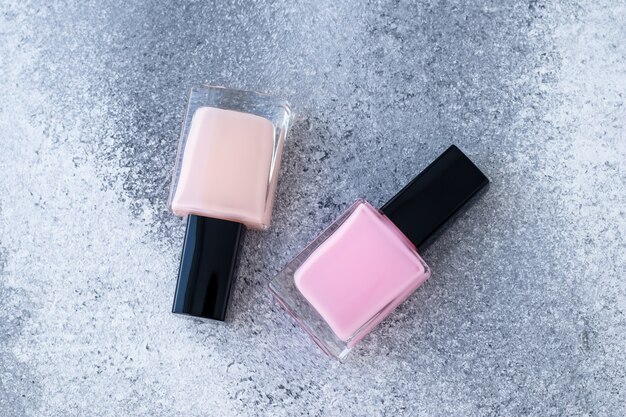 Two glass bottles of nail polish. Neutral beige and pink enamel on gray background.