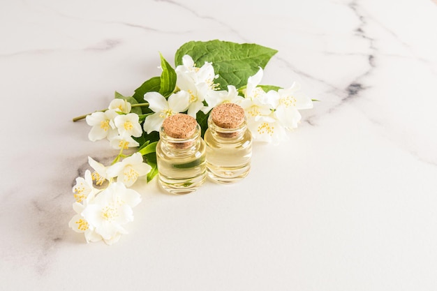 Two glass bottles with a cork lid with fragrant natural jasmine oil on the background of white jasmine flowers marble background a copy space