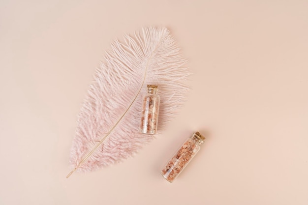 Two glass bottles with pink sea salt for spa procedures for face or body lying on a pink background