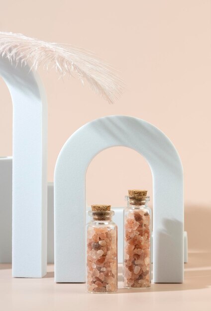 Two glass bottles with pink sea salt for spa procedures for face or body standing between geometric forms