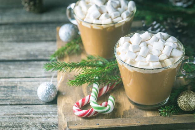 Two glass cups of cocoa with marshmallow on a wooden with christmas decorations