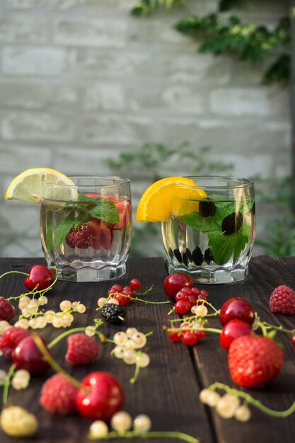 Two glass cups with drink of mint and berries are on the dark boards on brick wall background