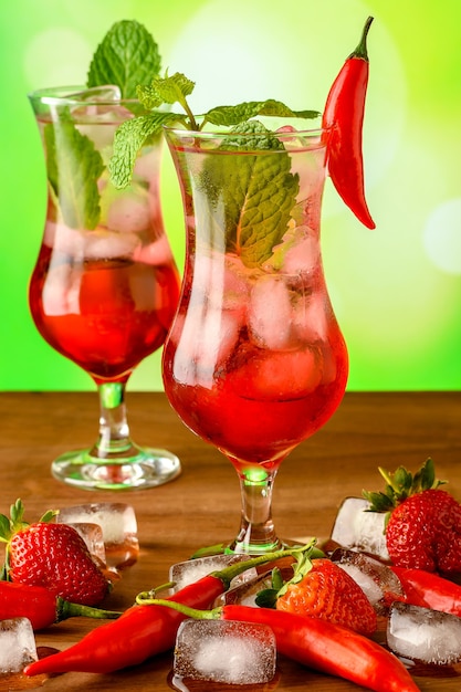 two glass glasses with grenadine cocktail decorated with pepper and mint on a wooden table