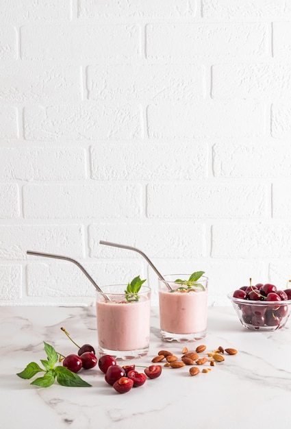 Two glass glasses with a natural organic ripe cherry smoothie with ecofriendly straw and a bowl of berries on a marble table Healthy eating