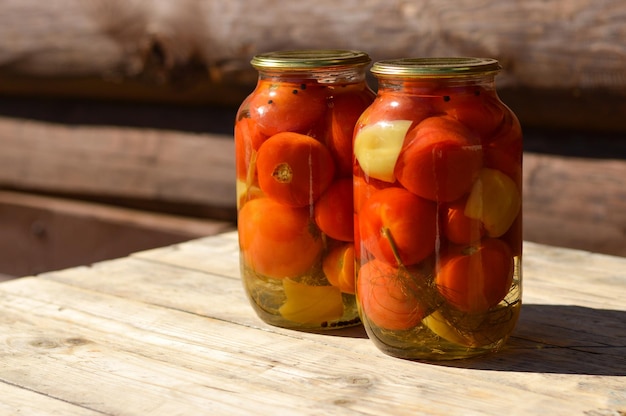 Two glass jars with canned tomatoes with iron lids stand on a wooden table home storage solution saving leftovers canning concept rustic composition