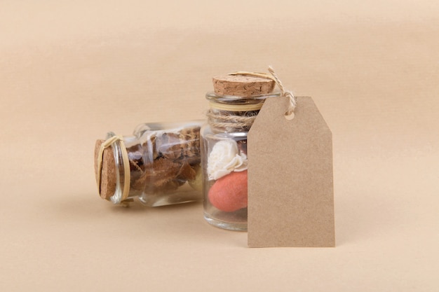 Two glass jars with dried herbs for aromatherapy with empty rectungolar tag on craft paper backrgound