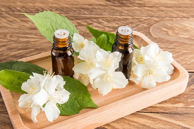 Two glass medical bottles of jasmine oil for selfcare the concept of spa and aromatherapy wooden background with the flowers of the plant