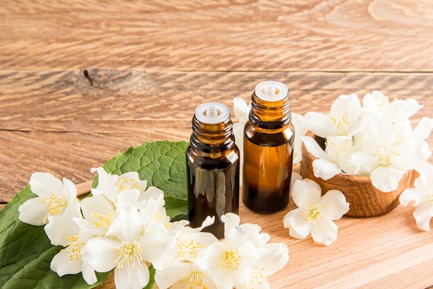 Two glass medical bottles of jasmine oil for selfcare the concept of spa and aromatherapy wooden background with the flowers of the plant