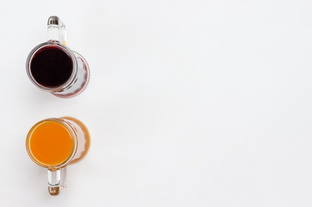 Photo two glass mugs with orange and burgundy beverages. white background. flat lay. abstract picture