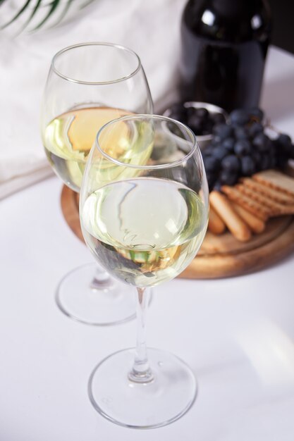 Two glass of white wine and plate with assorted cheese, fruit and other snacks for party