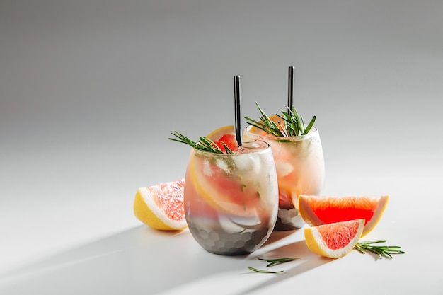 Два бокала с коктейлем из грейпфрута и розмарина. Летние напитки со свежими цитрусовыми и льдом.