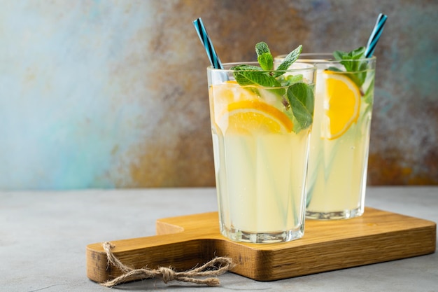 Two glass with lemonade or mojito cocktail with lemon and mint cold refreshing drink or beverage with ice on rustic blue background Copy space
