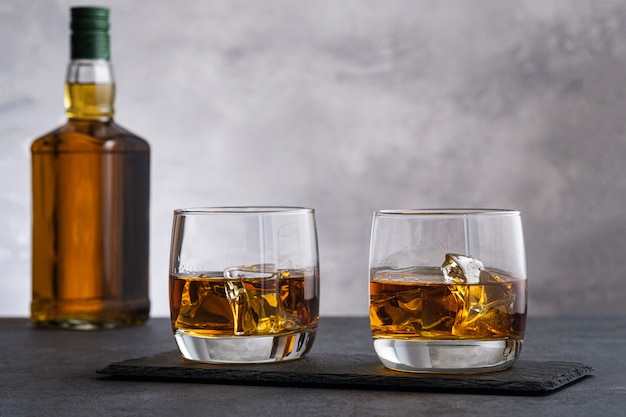 Two glass with whiskey and ice cubes on wall bottle