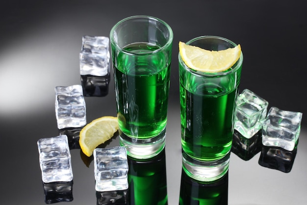 Two glasses of absinthe lemon and ice on grey background